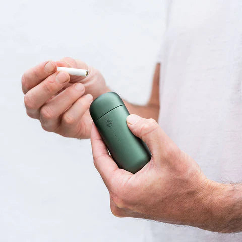 Hände halten grünes Omura-Gerät und Cannabis Stick. 